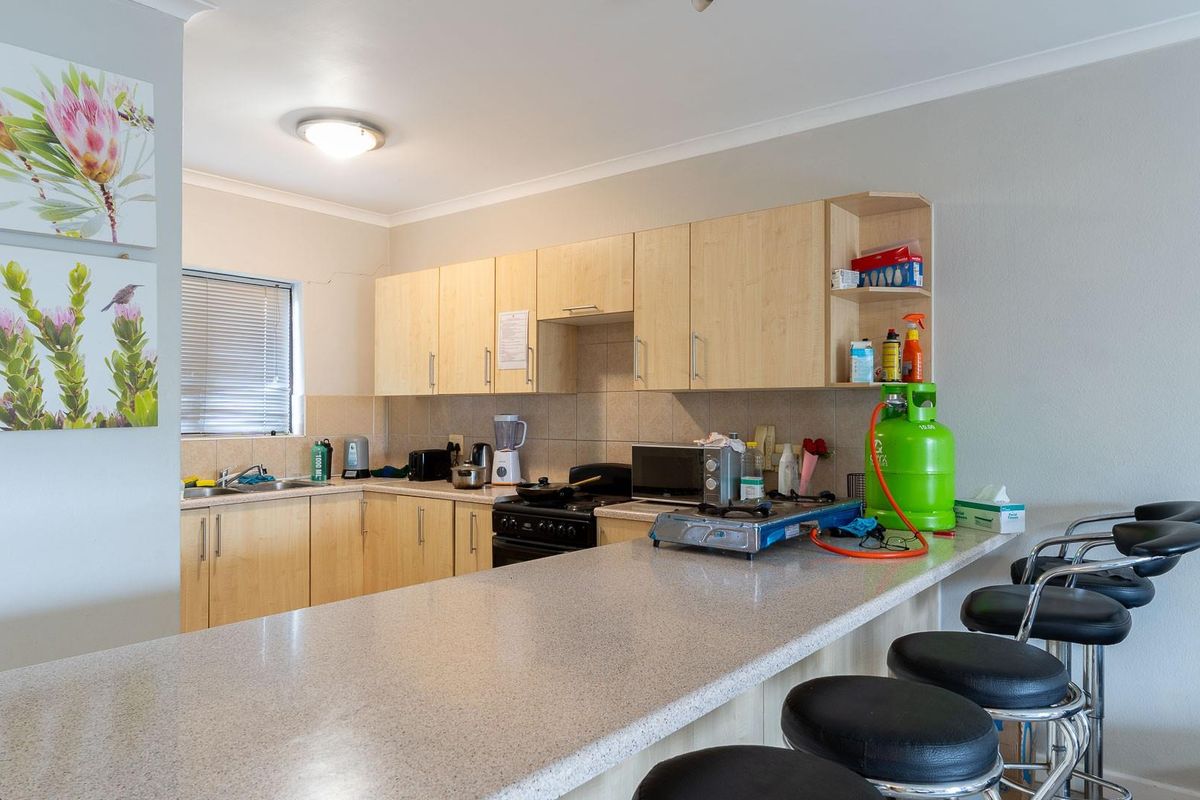 Functional kitchen featuring light wood-finish cabinetry, a breakfast bar counter, tiled backsplash, and a freestanding stove with integrated sink area.