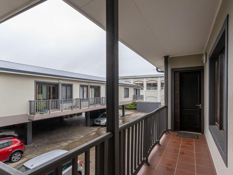 A covered balcony with tiled flooring and metal railings, overlooking the apartment complex parking area.