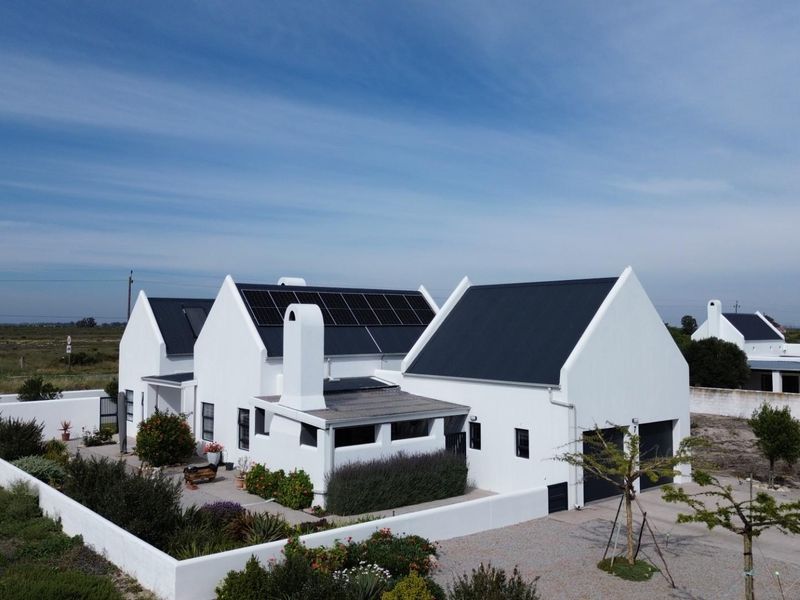 Aerial view of a modern white house with a dark metal roof, solar panels, and a secure walled garden area.