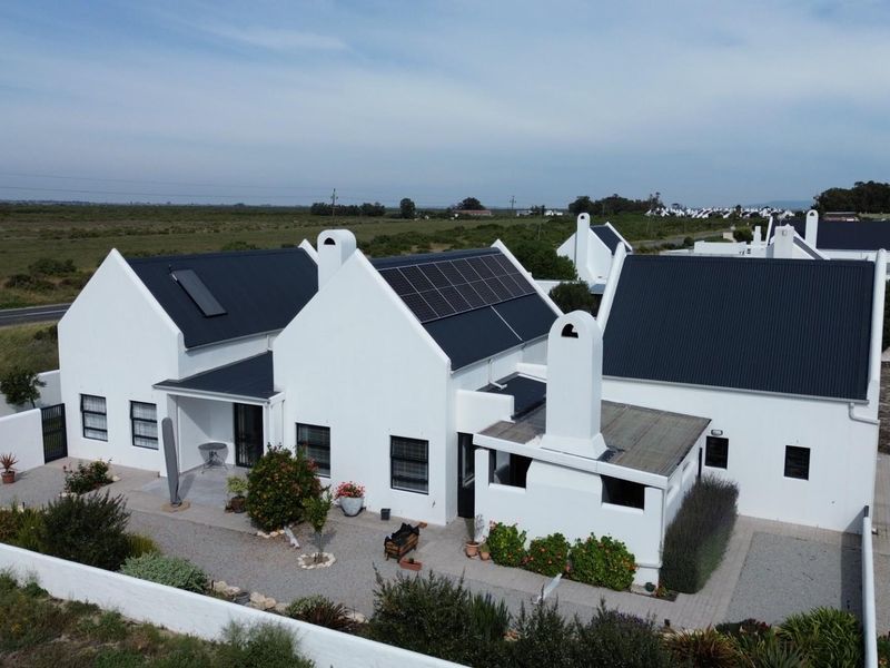 Aerial view of a modern white house with a dark metal roof, solar panels, and a private paved courtyard area.