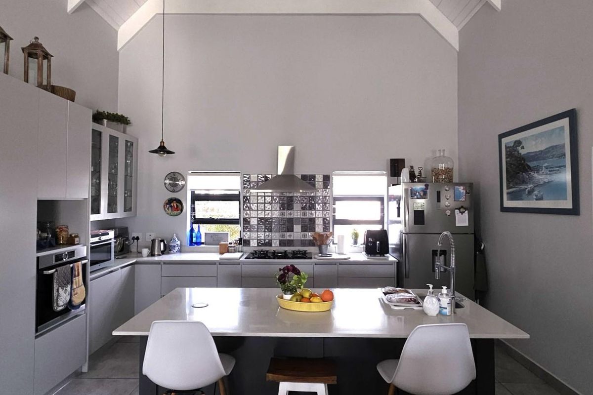Modern kitchen featuring a central island, stone countertops, built-in oven, gas hob, and a striking vaulted ceiling with contemporary finishes.