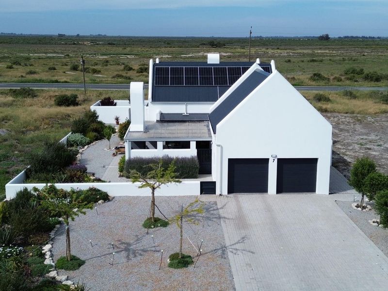 Aerial view of a modern white house featuring a double garage, solar panels, and a landscaped garden in a rural setting.