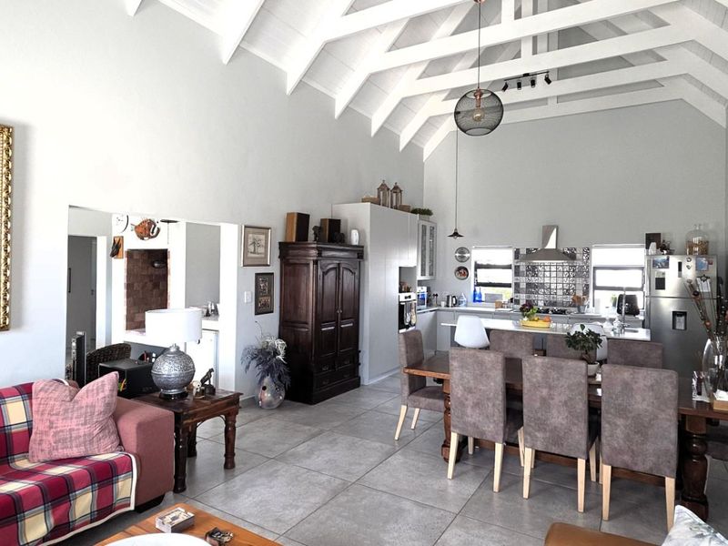 Spacious open-plan living and dining area featuring high vaulted ceilings with exposed rafters, tiled flooring, and a modern kitchen with a central island.