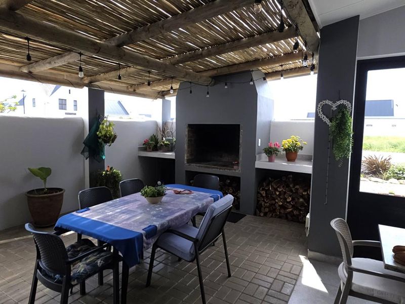 Covered outdoor patio featuring a built-in braai, thatched roof, and paved flooring, ideal for alfresco dining and entertaining.