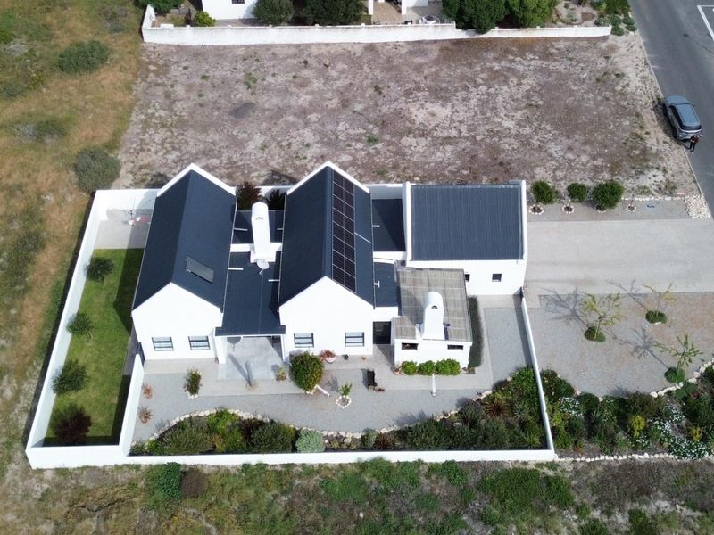 Aerial view of a modern house featuring a dark metal roof with integrated solar panels, a chimney, and a well-maintained garden with boundary walls.