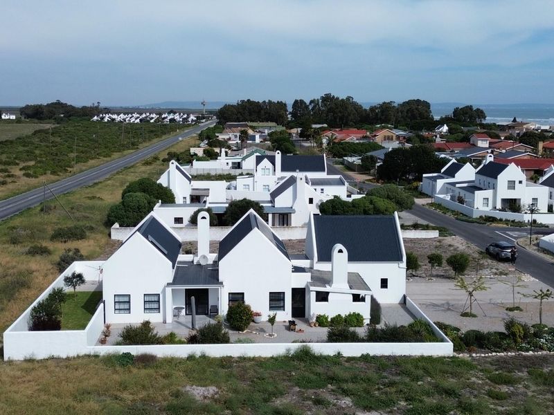 Aerial view of a modern white house with a pitched roof, featuring a boundary wall and paved driveway in a coastal residential estate.