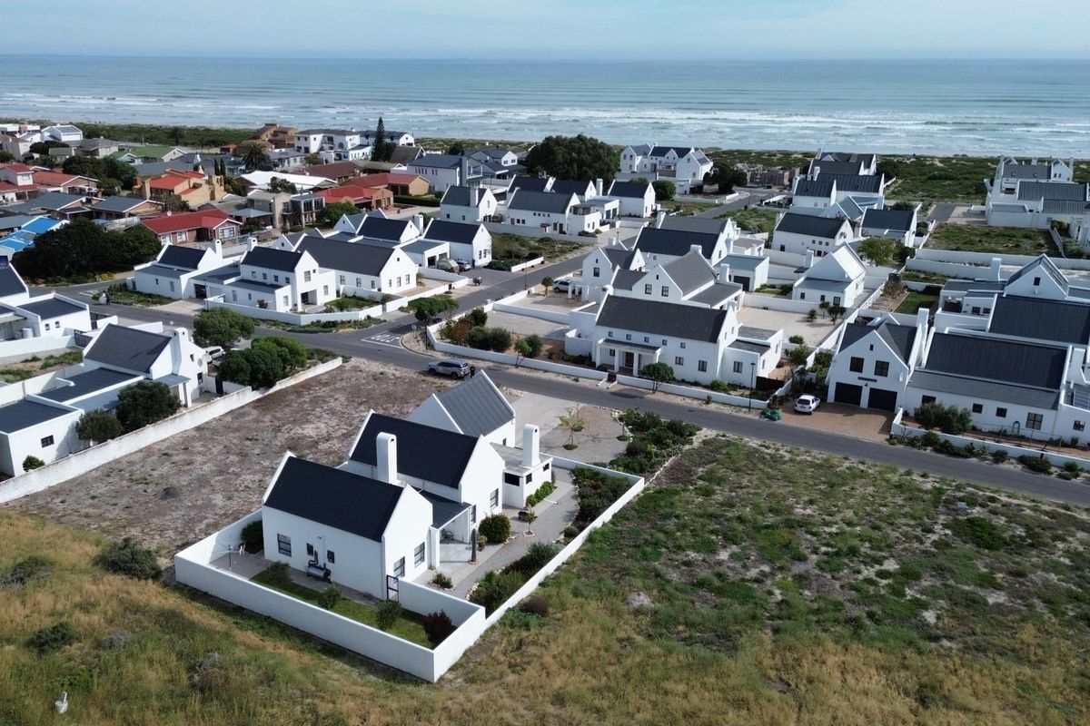 Aerial view of a coastal residential estate featuring white houses with dark roofs, situated near the ocean.
