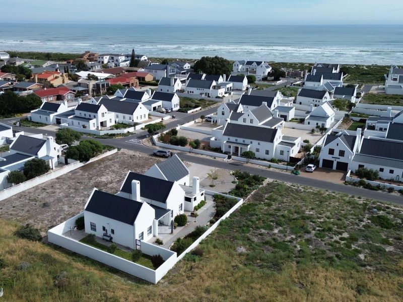 Aerial view of a coastal residential estate featuring white houses with dark roofs, situated near the ocean.