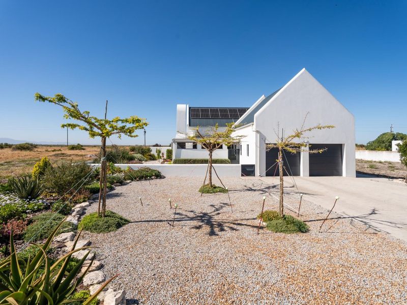 Modern white house with a pitched roof, solar panels, double garage, and a landscaped gravel garden with young trees.