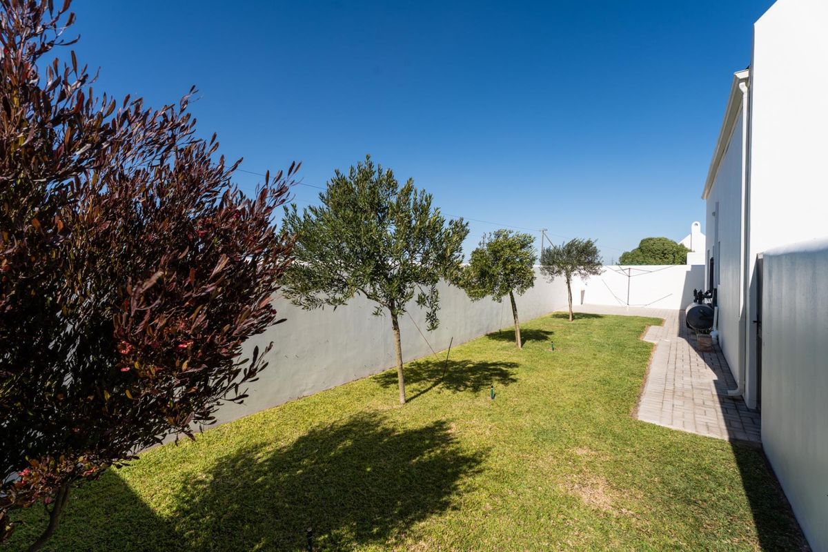 A well-maintained rear garden featuring a paved walkway, manicured lawn, and perimeter boundary walls.