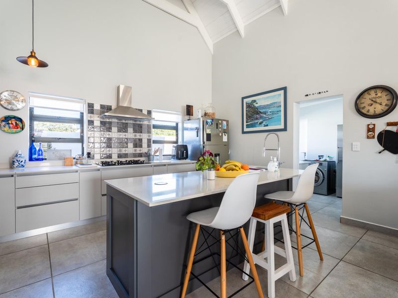 Modern kitchen featuring a central island with stone countertops, gas hob, stainless steel extractor, and vaulted ceilings, with an adjacent laundry area.