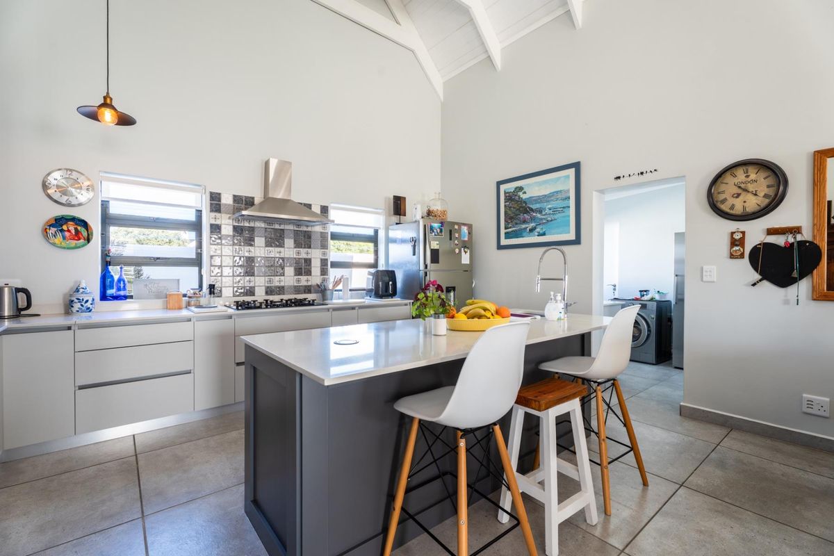 Modern kitchen featuring a central island with stone countertops, gas hob, stainless steel extractor, and vaulted ceilings, with an adjacent laundry area.