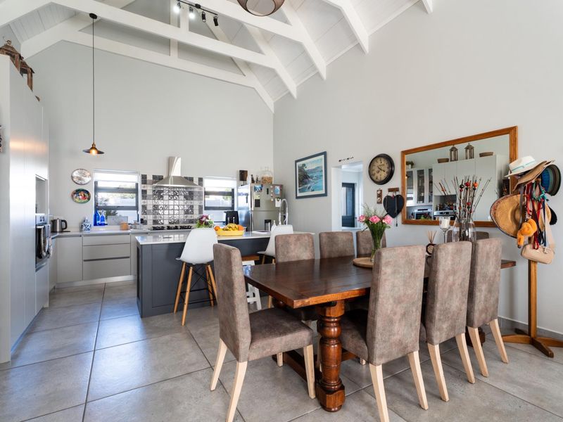 Spacious open-plan kitchen and dining area featuring vaulted ceilings with exposed rafters, modern cabinetry, a central island, and large format floor tiles.