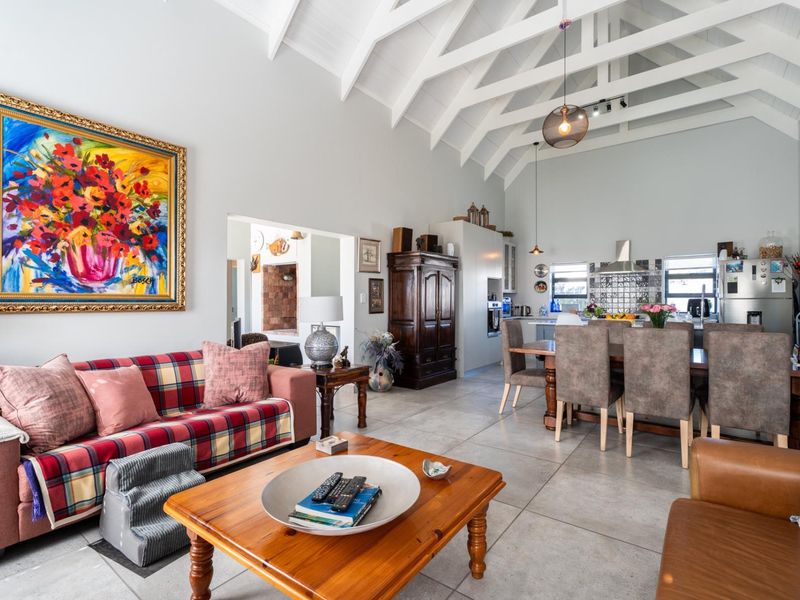 Spacious open-plan living and dining area featuring high vaulted ceilings with exposed rafters and modern tiled flooring, seamlessly connected to a functional kitchen.