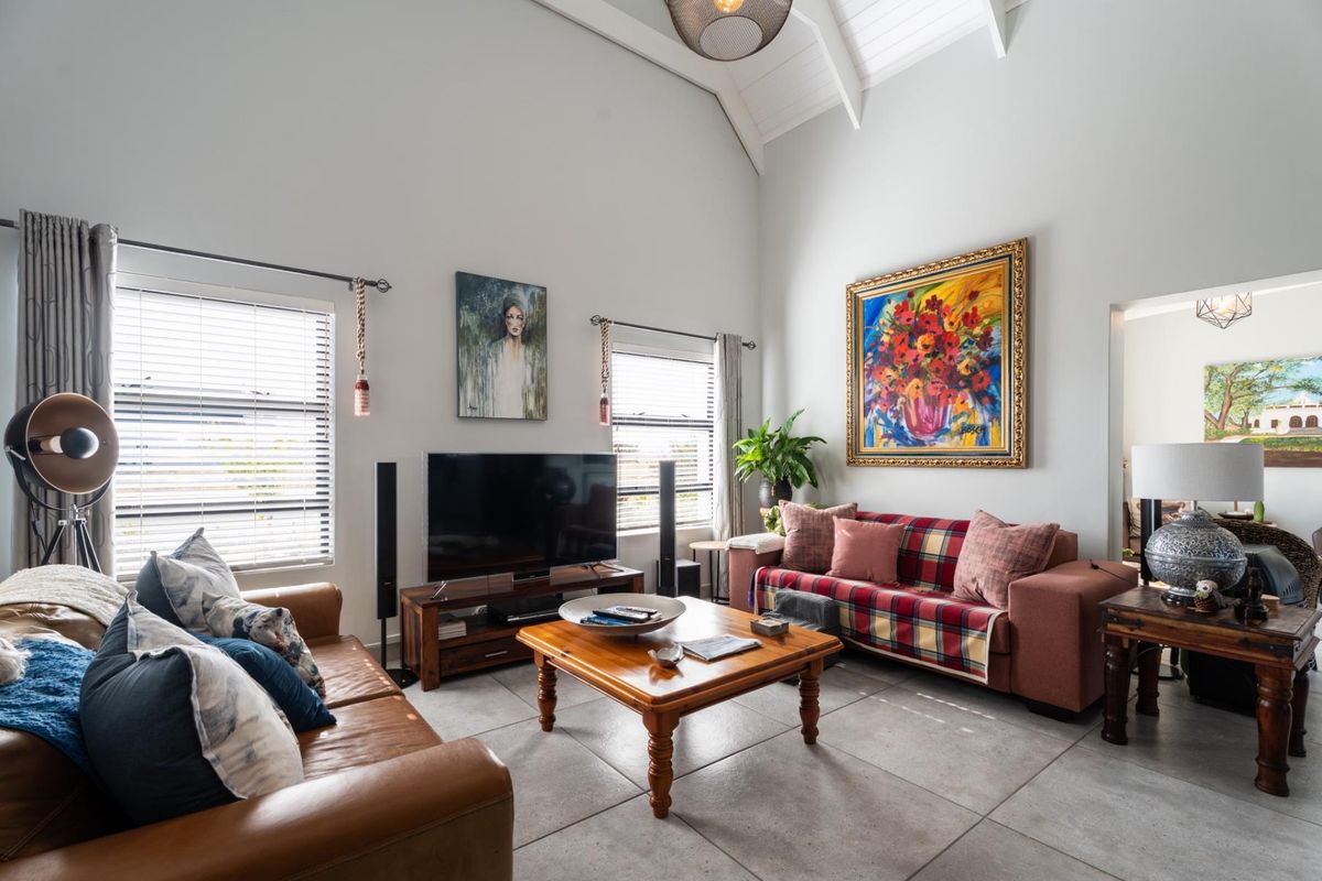 Spacious living room featuring high vaulted ceilings with exposed rafters, large windows with venetian blinds, and neutral tiled flooring.
