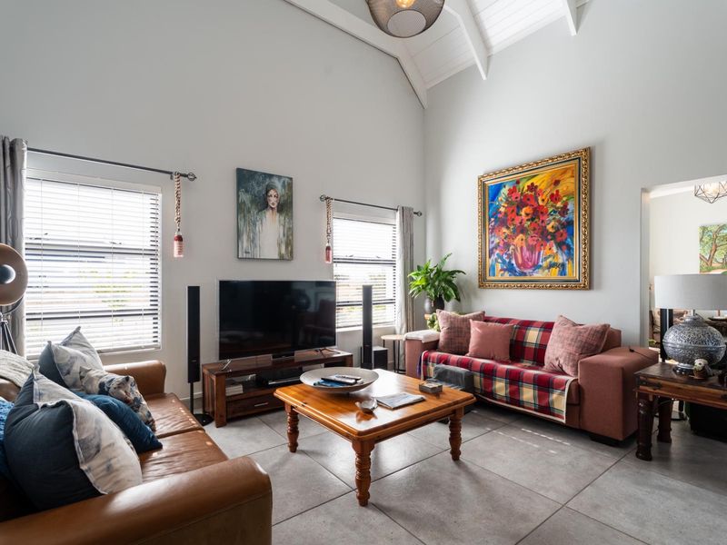 Spacious living room featuring high vaulted ceilings with exposed rafters, large windows with venetian blinds, and neutral tiled flooring.