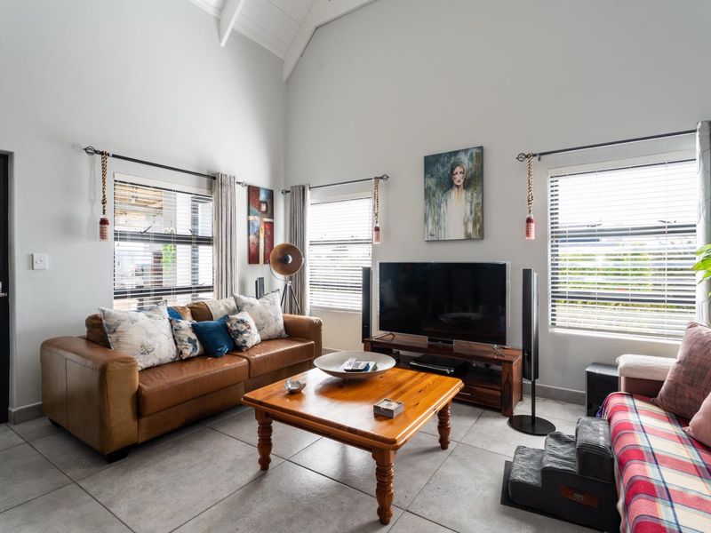 A bright living room featuring high vaulted ceilings, large windows with venetian blinds, and neutral tiled flooring.