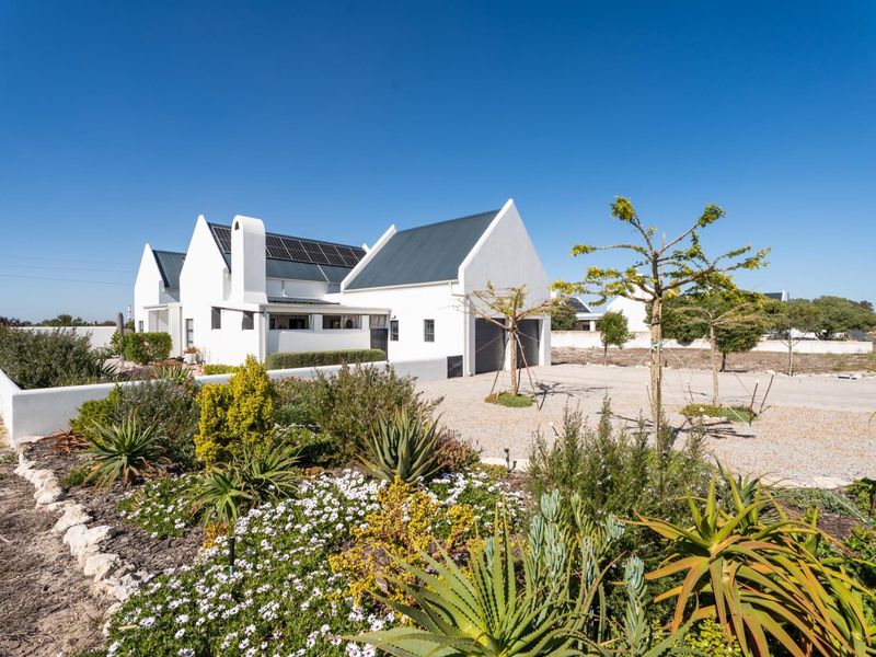 A modern white gabled house featuring solar panels, a gravel driveway, and a well-maintained landscaped garden in a sunny setting.