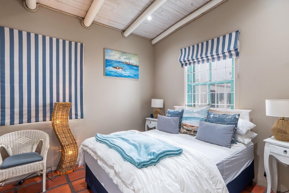 A cozy bedroom featuring exposed beam ceilings, terracotta tile flooring, and a multi-pane window with a nautical-themed aesthetic.