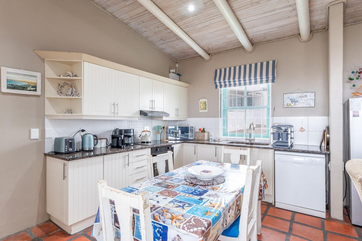 A functional kitchen featuring white cabinetry, dark countertops, a tiled backsplash, and exposed wooden beams on the ceiling with terracotta flooring.
