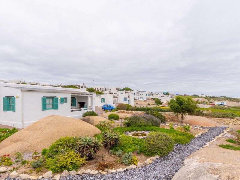 A well-maintained coastal property featuring a landscaped garden with natural stone boulders, a gravel pathway, and a covered patio area.