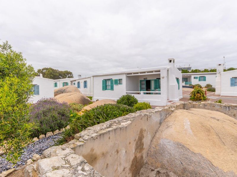 A view of the rear exterior of the property featuring a covered patio, stone retaining walls, and landscaped garden areas with natural rock formations.