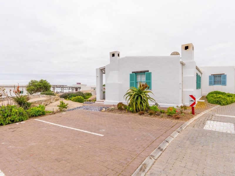 A charming white cottage-style home featuring blue shutters, dual chimneys, and a paved driveway, situated in a coastal setting.