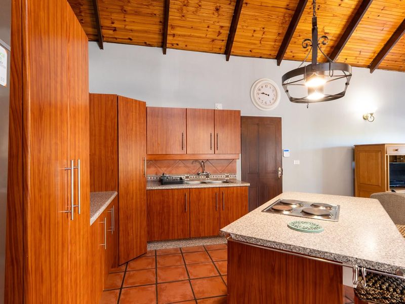 A spacious kitchen featuring wooden vaulted ceilings, built-in cabinetry, granite countertops, a central island with an electric hob, and terracotta tiled flooring.