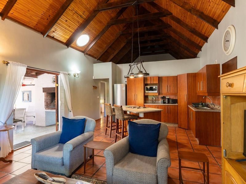 Open-plan living and kitchen area featuring a high vaulted timber ceiling, terracotta flooring, and functional wooden cabinetry with a central island.