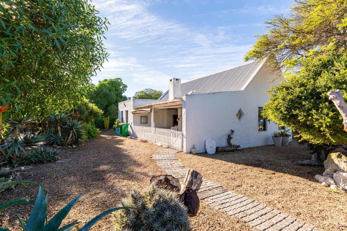 A view of the rear exterior of the house featuring a white masonry facade, corrugated metal roof, and a stone pathway leading to a patio.