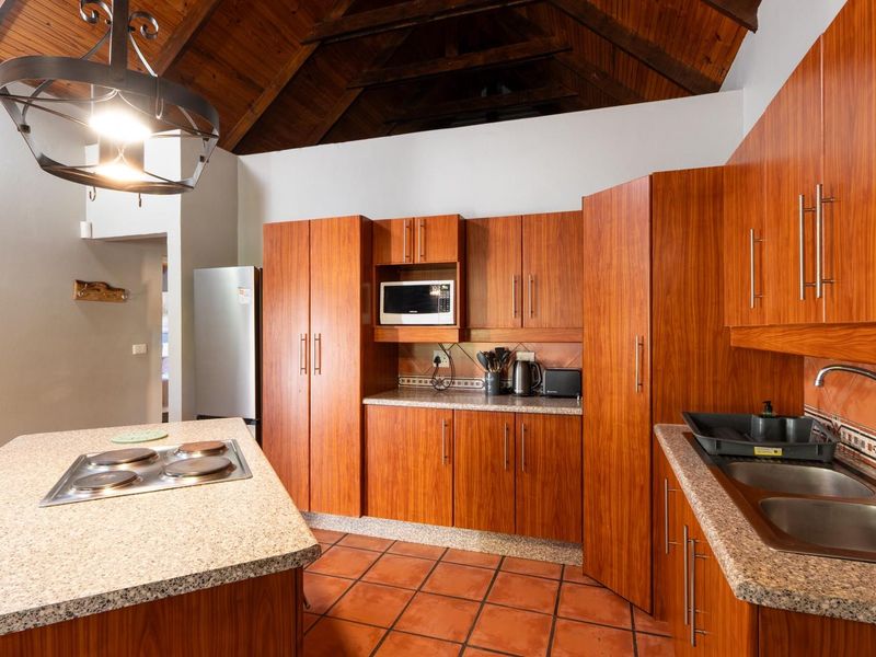 Spacious kitchen featuring warm wood cabinetry, granite countertops, a central island with a built-in hob, and a striking exposed timber vaulted ceiling.