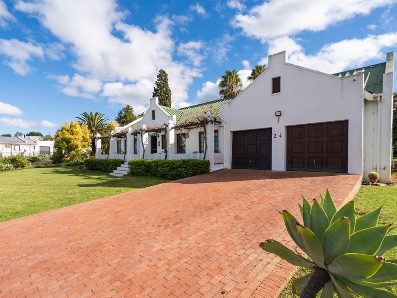 Charming Cape Dutch style home featuring a brick driveway, double garage, and a well-maintained front garden with a pergola.