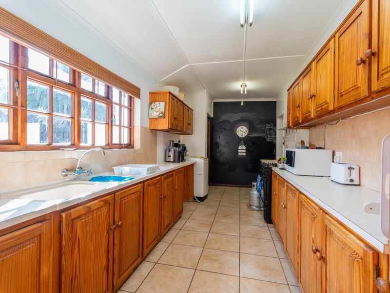 A functional galley-style kitchen featuring extensive wooden cabinetry, tiled flooring, and a tiled backsplash with ample natural light from the side windows.