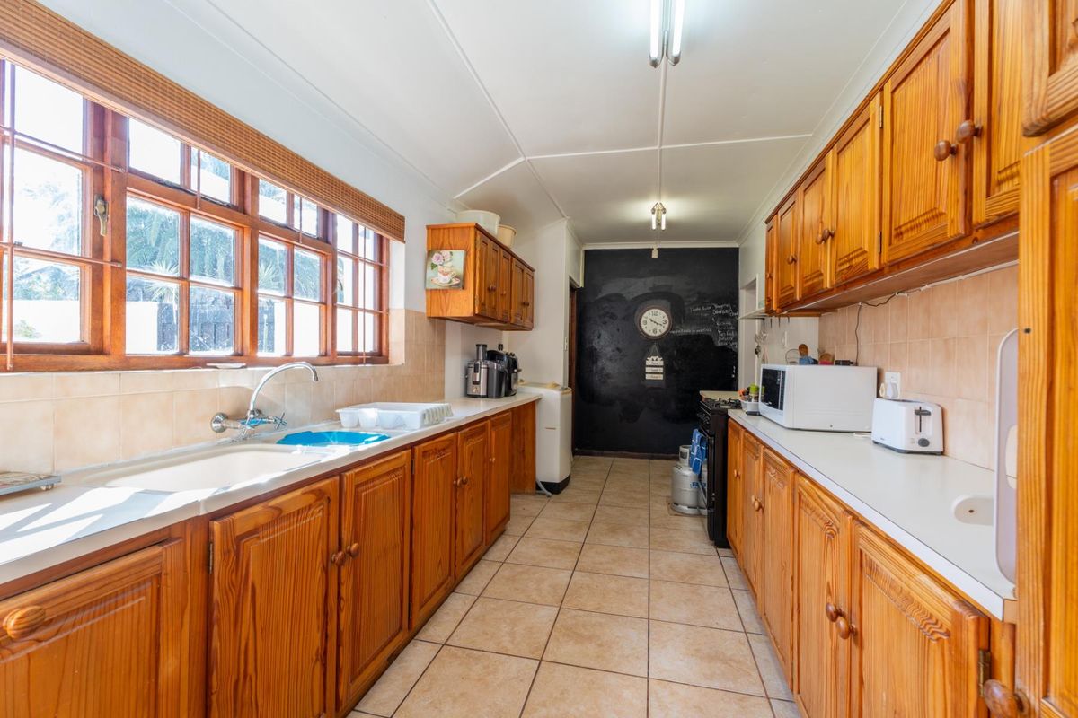 A functional galley-style kitchen featuring extensive wooden cabinetry, tiled flooring, and a tiled backsplash with ample natural light from the side windows.