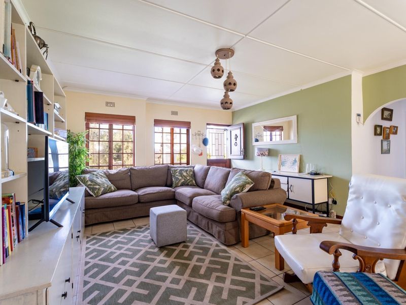 A comfortable living room featuring tiled flooring, built-in shelving, and natural light through timber-framed windows, leading into an adjacent space via an archway.