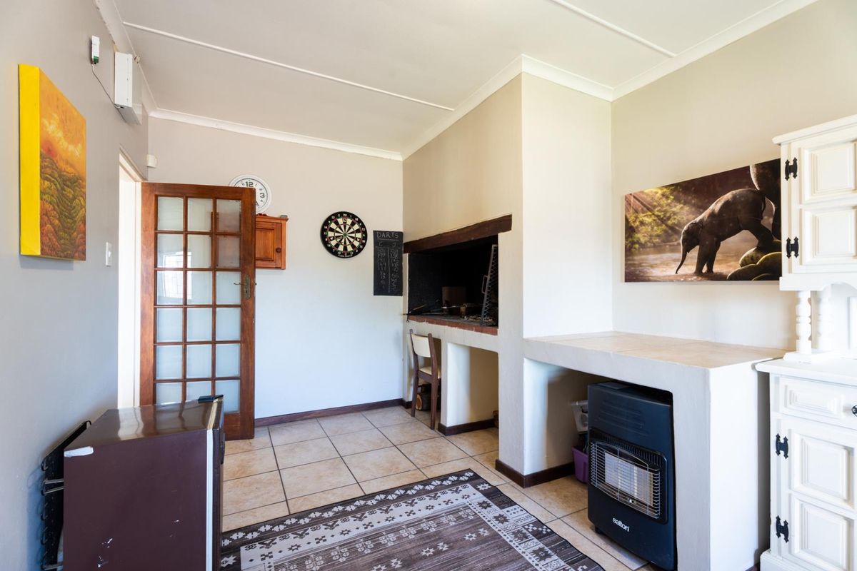 A living area featuring a built-in braai, tiled flooring, and a classic timber-framed glass door, offering a functional space for indoor entertaining.