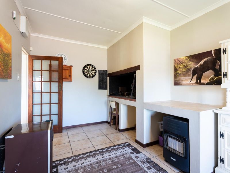 A living area featuring a built-in braai, tiled flooring, and a classic timber-framed glass door, offering a functional space for indoor entertaining.