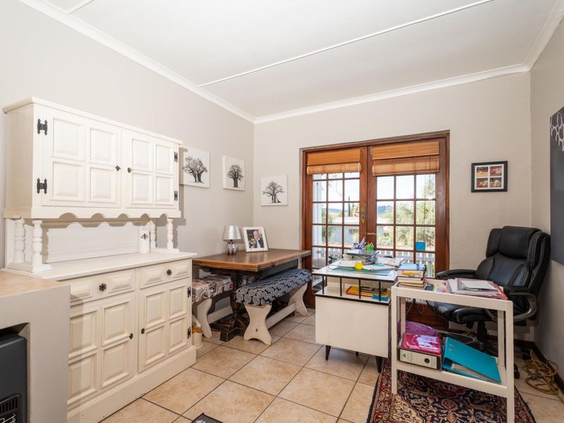 A functional home office space featuring tiled flooring and timber-framed glass double doors providing natural light and outdoor access.