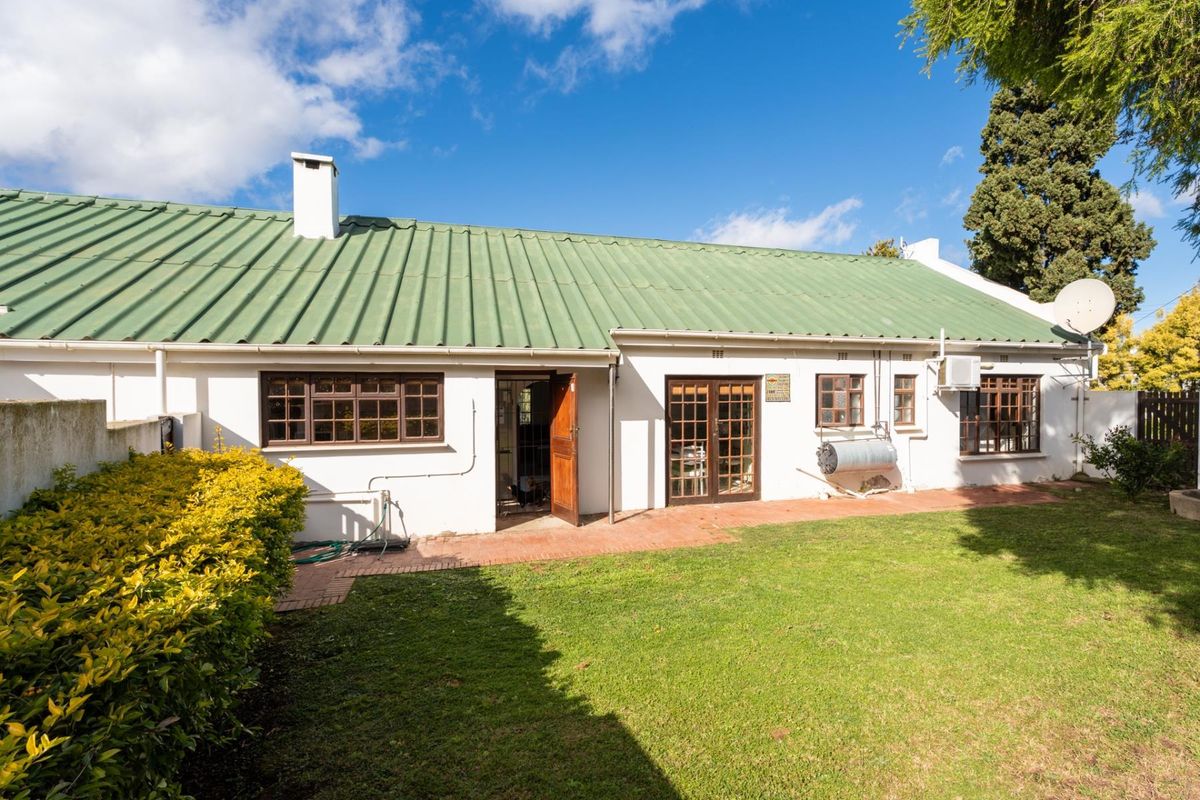 Rear view of the house featuring a green corrugated metal roof, brick patio, and established garden area.