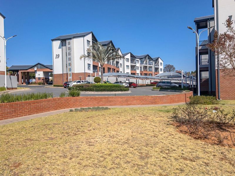 A view of the apartment complex exterior featuring multi-story buildings, paved driveway, covered parking, and landscaped garden areas.