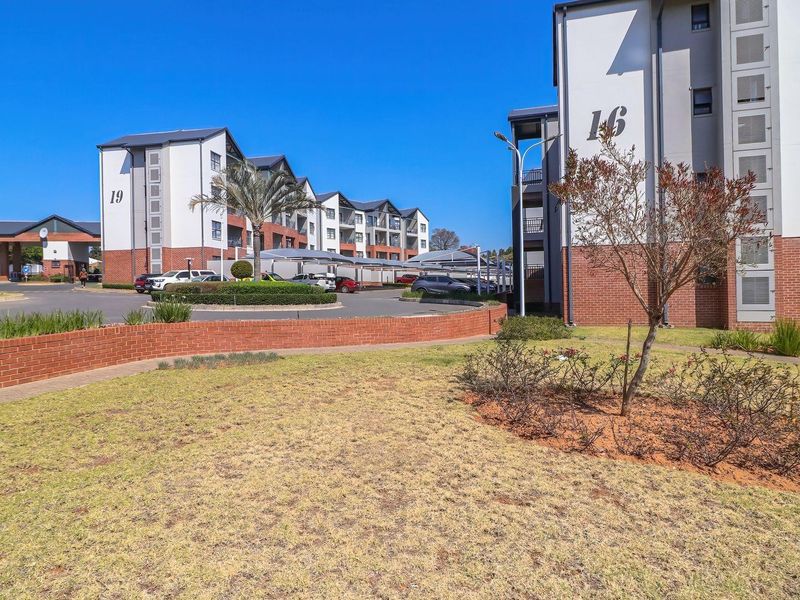 View of the apartment complex exterior featuring landscaped gardens, paved driveways, and covered parking structures between the residential buildings.