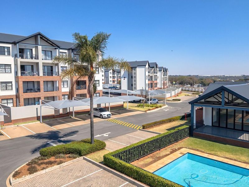 Aerial view of a modern apartment complex featuring a swimming pool, landscaped gardens, and covered parking bays.