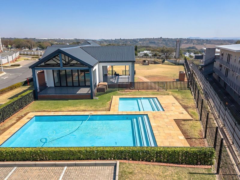 Aerial view of a communal apartment complex pool area featuring a swimming pool, paved deck, and adjacent clubhouse facility.
