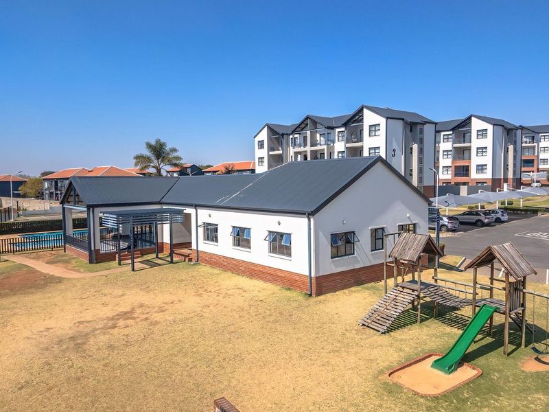 Aerial view of the apartment complex grounds, featuring a communal building with a covered patio, playground area, and adjacent parking facilities.