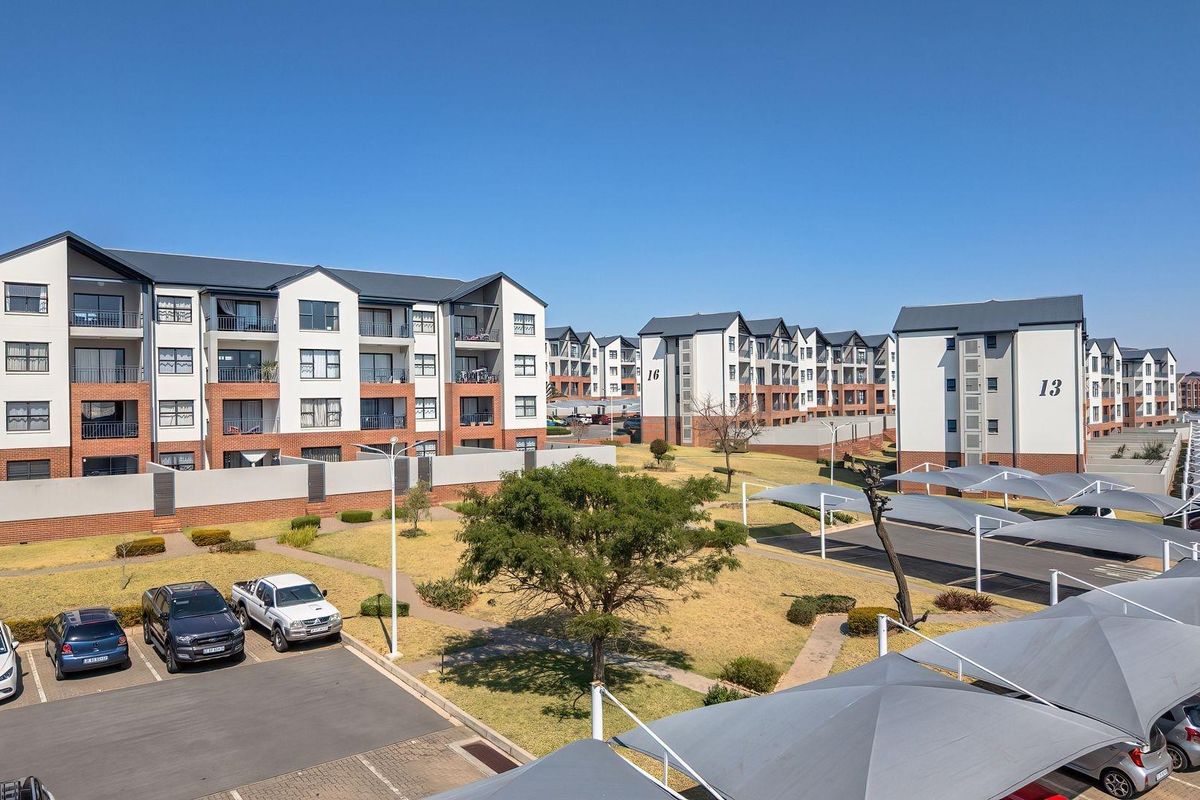 Aerial view of a modern apartment complex featuring multi-story residential buildings, landscaped grounds, paved parking areas, and covered shade cloth carports.