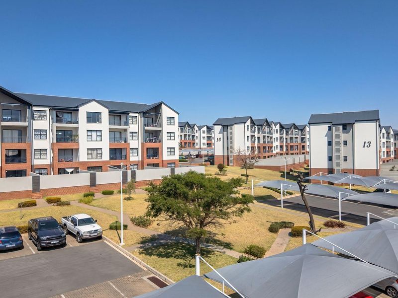 Aerial view of a modern apartment complex featuring multi-story residential buildings, landscaped grounds, paved parking areas, and covered shade cloth carports.