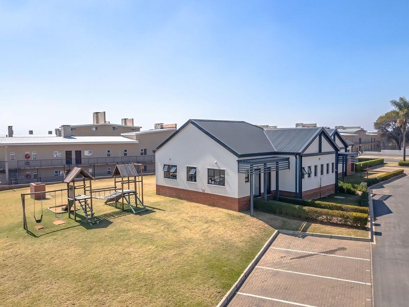 Aerial view of the apartment complex featuring a communal playground, landscaped garden areas, and dedicated paved parking bays.