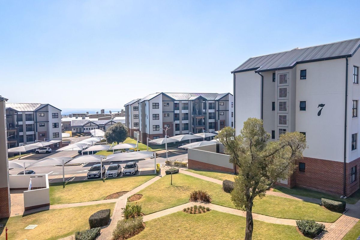 An elevated aerial view of a modern apartment complex featuring landscaped gardens, paved walkways, and covered parking bays.