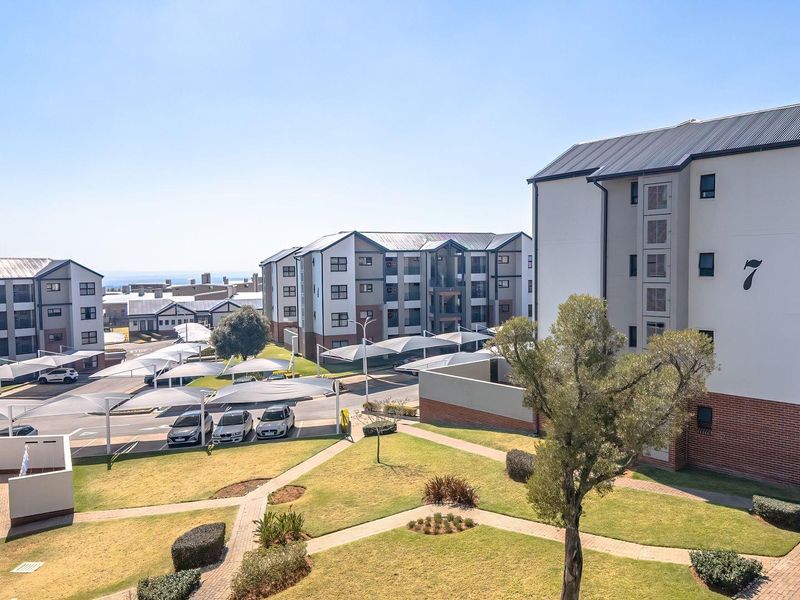 An elevated aerial view of a modern apartment complex featuring landscaped gardens, paved walkways, and covered parking bays.
