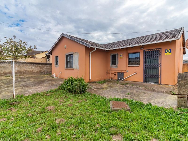 Rear view of the house featuring a concrete patio area, security gates, and perimeter walling, showing signs of wear and weathering.